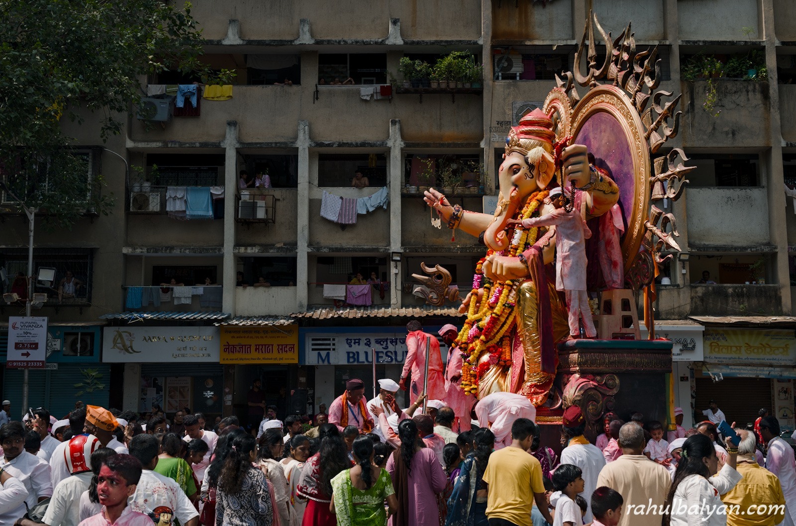 Giant Ganesha idol passes an old chawl building as residents watch from balconies above the crowd