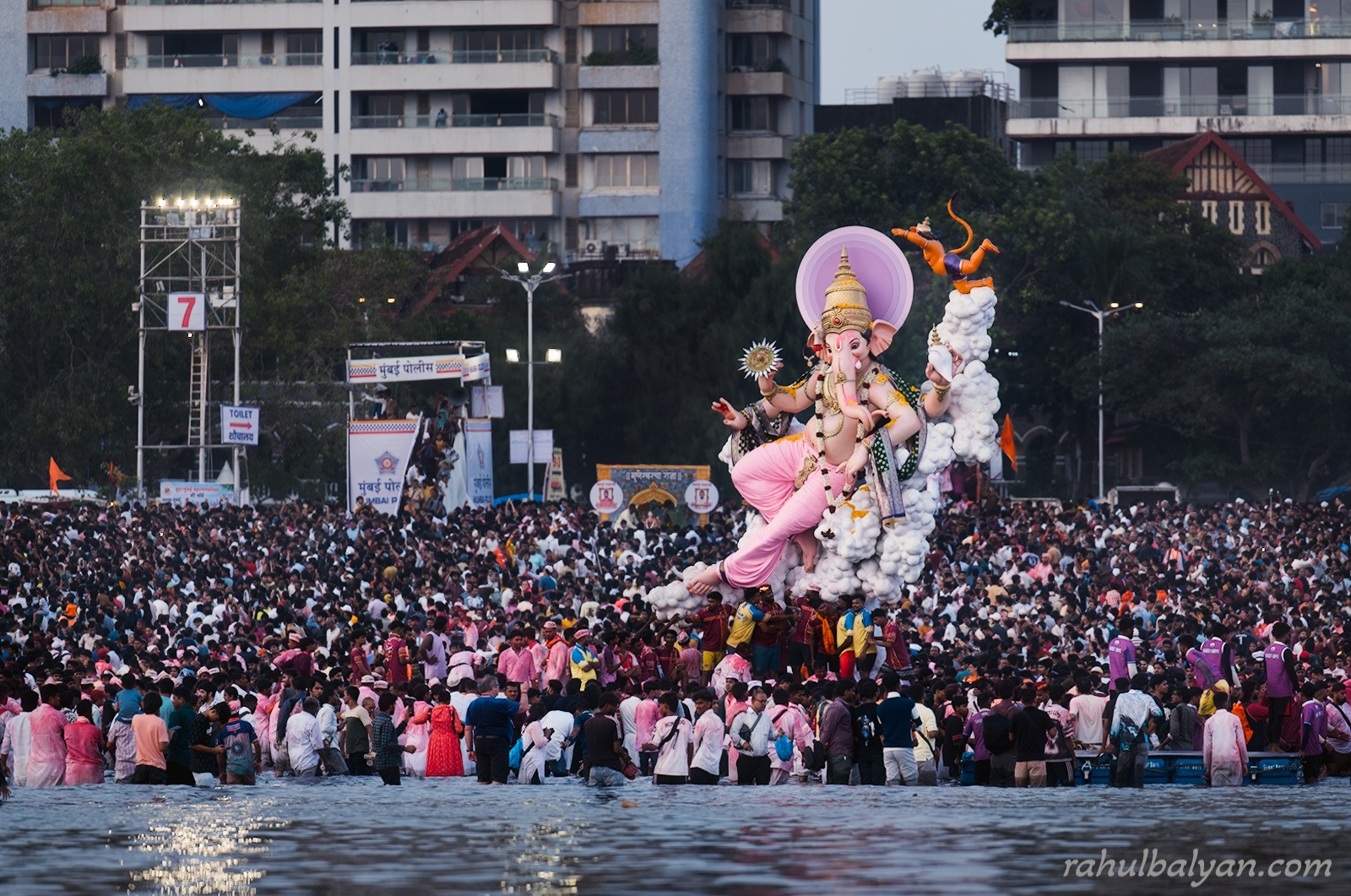 Ganesha idol on a cloud-shaped throne moving through a crowd in the sea at dusk